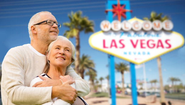 retirement, vacation, tourism and travel concept - happy senior couple hugging over welcome to fabulous las vegas sign background